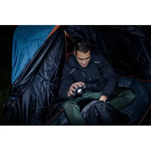 Arbeidslys LED, vist i bruk av mann som organiserer utstyr i mørkt telt med blå og svarte paneler.