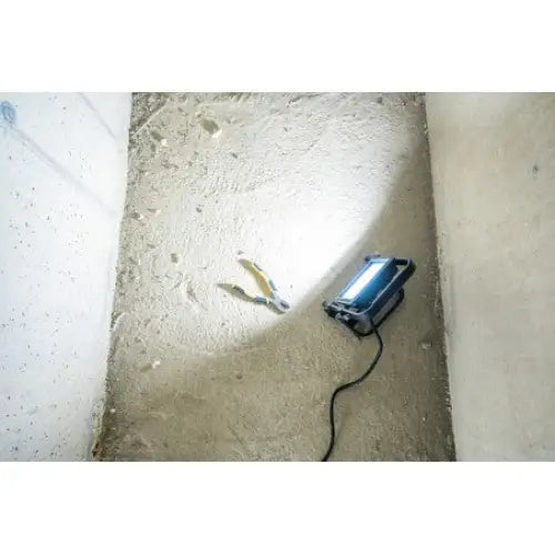 Arbeidslys LED JARO 4060 M, blått lys på betonggulv og gulthåndtaket verktøy, sett fra toppen i romhjørne.