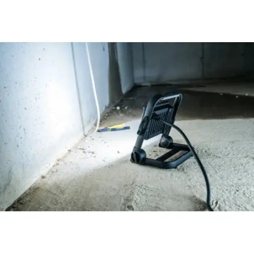 Arbeidslampe LED JARO 4060 M, sidevisning med lys mot betongvegg og synlig strømkabel på støvete gulv.