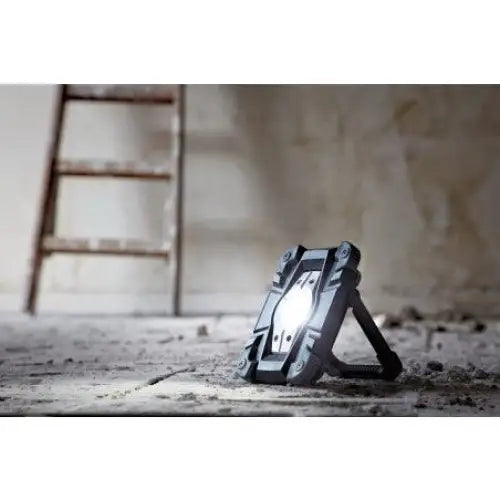 Arbeidslampe LED RUFUS i sort plast og metall, lyser opp betonggulv foran stige og oppussingsvegg.