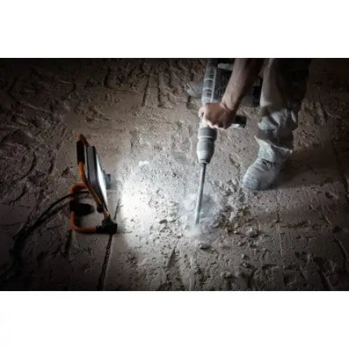 Arbeidslys SLIM LED 950lm i bruk, lyser opp støvete gulv mens det bores i betong med slagbormaskin.
