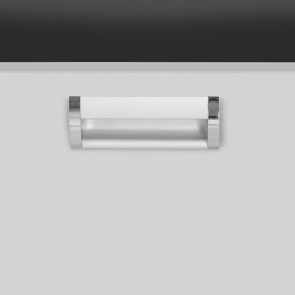 Sølvfarget metallhåndtak på arbeidsbenk, frontvisning mot lys skuffeflate med mørk toppkant.