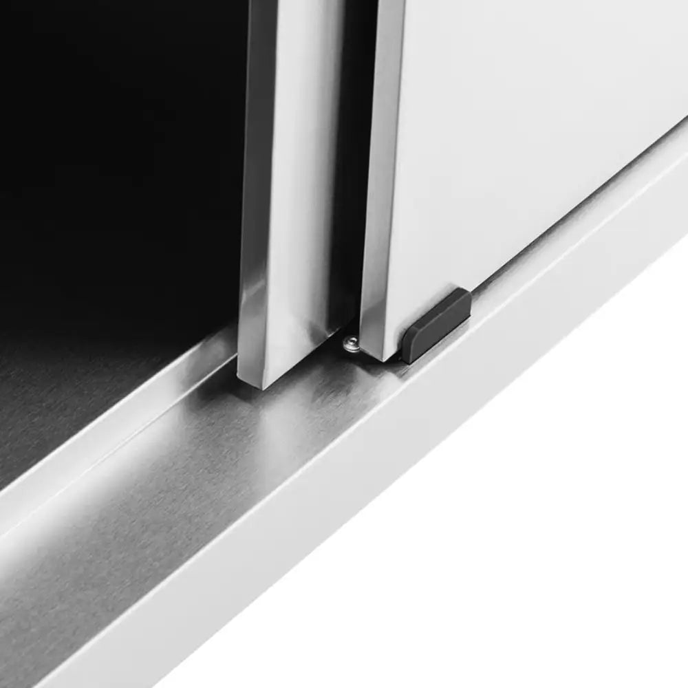 Arbeidsbenk i børstet stål, nærbilde av skyvedørens skinne og plaststopp i skapets hjørne.