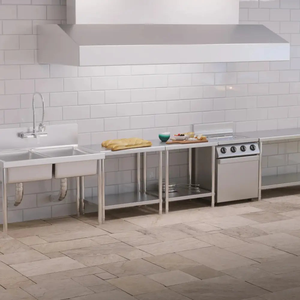 Arbeidsbenkeplate med sentral stålhyller, doble vasker og kjøkkenutstyr i et industrikjøkken.