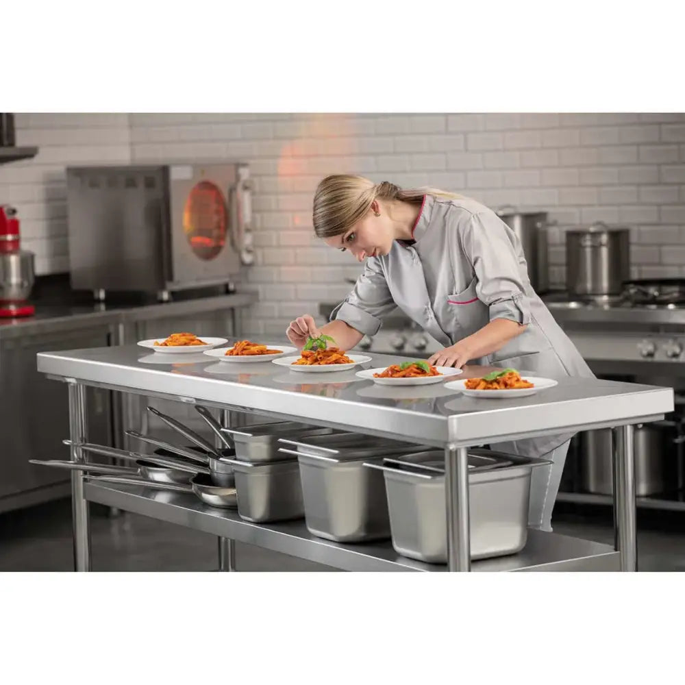 Arbeidsbord sentral i rustfritt stål, sidevisning med kokk som pynter mat og gryter oppbevart under benken.