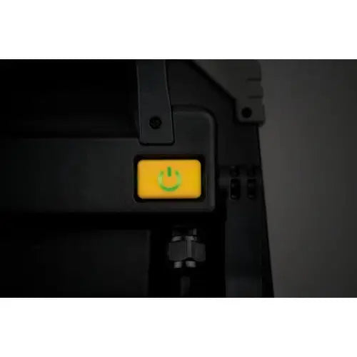 Arbeidslys LED DINORA, nærbilde av gul knapp med grønt på/av-symbol på svart overflate.