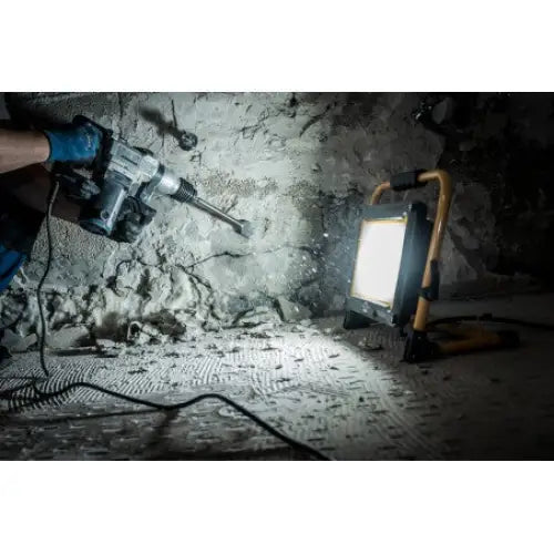 Arbeidslys LED JARO 7050 M, sidevisning i bruk, lyser opp murvegg mens det bores i byggeprosjekt.