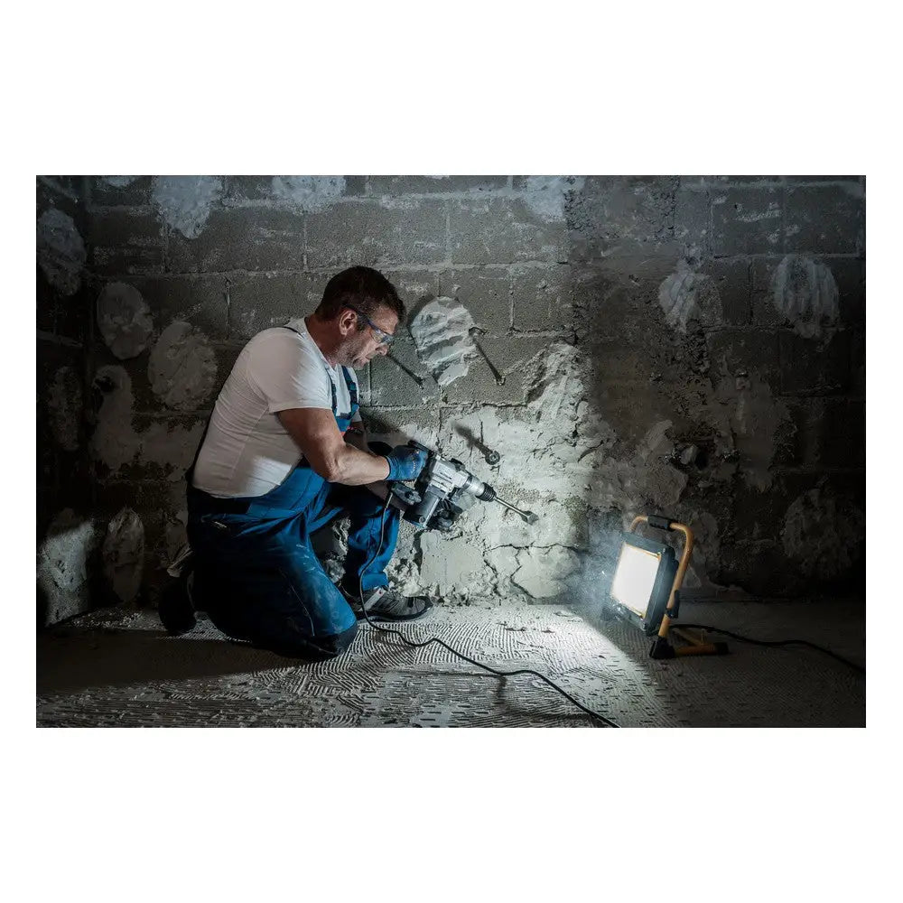 Arbeidslys LED JARO 7050 M i bruk, lyser opp murvegg mens håndverker borer i mørkt rom.