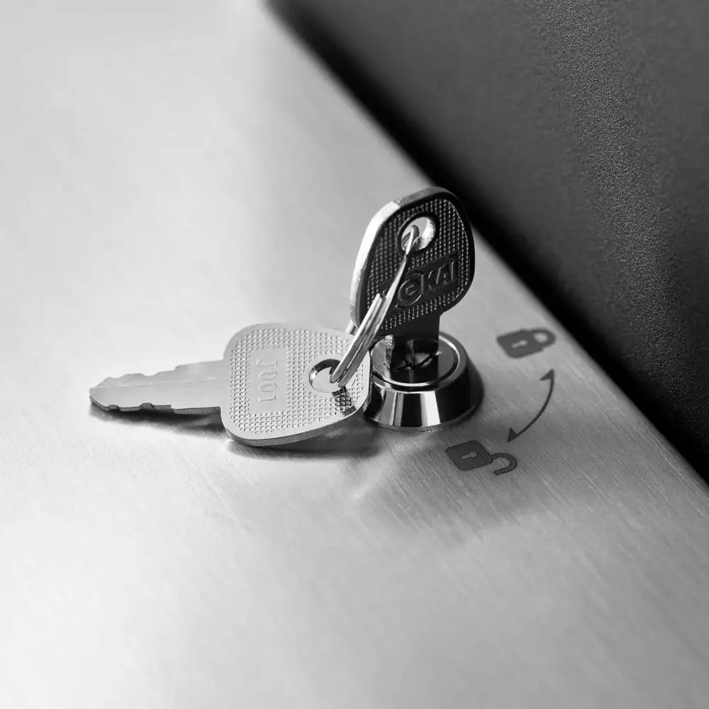 To sølvfargede nøkler i sylinderlås på børstet metall med tydelige låse- og åpnesymboler.