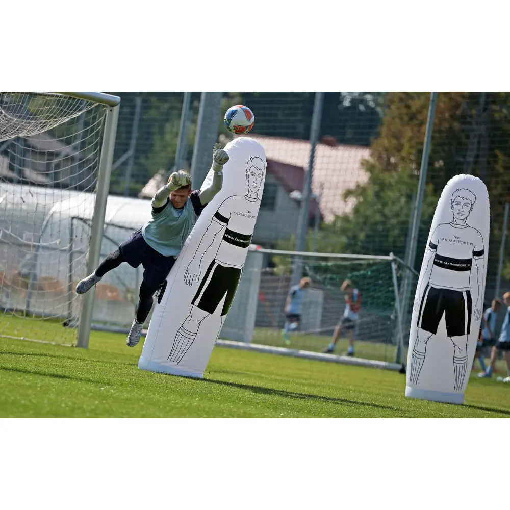 Autooppblåsbar fotballfigur brukt som hinder på gressbane, keeper i aksjon foran mål under trening.