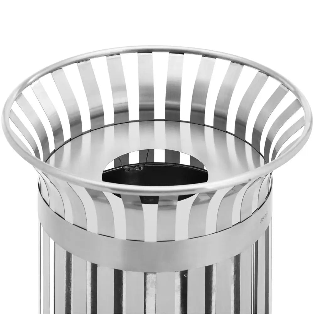 Avfallskurv i sølvfarget stål, nærbilde av topplokk med vertikale utskjæringer og sentral rund åpning.