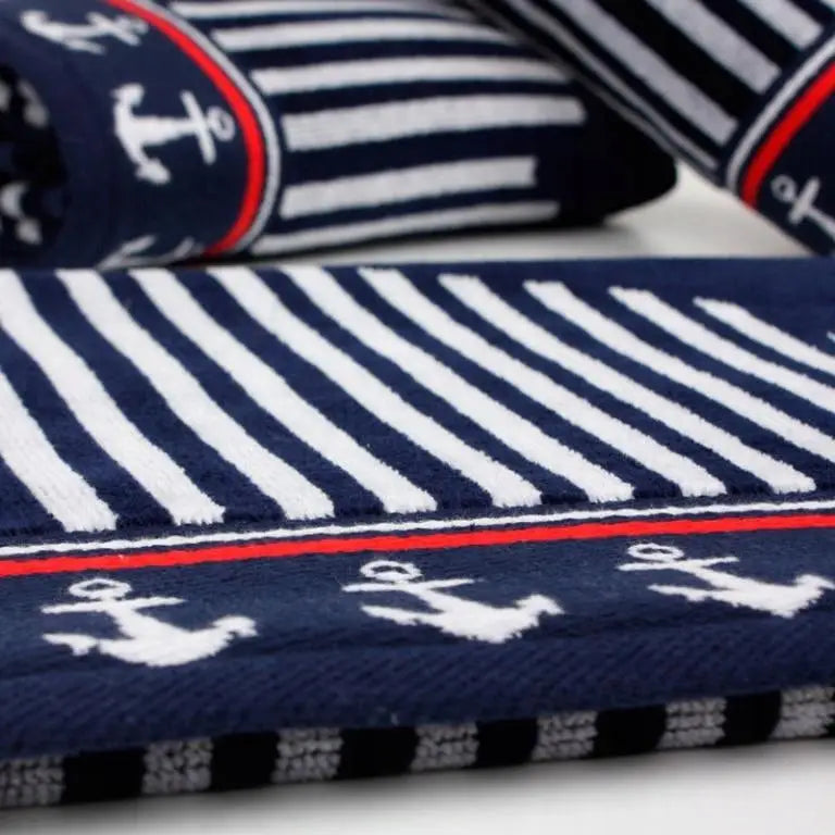 Marineblått strandhåndkle i bomull med hvite ankre, røde og hvite striper, nærbilde fra skrå vinkel.