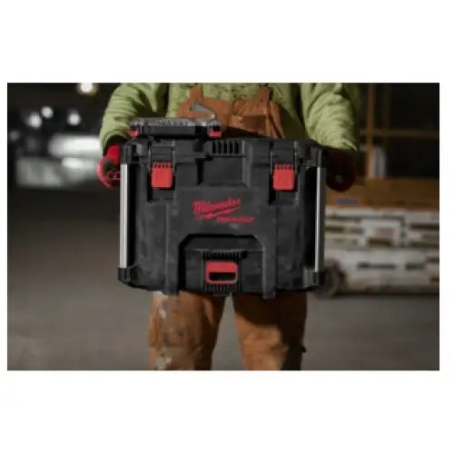 Bærbar verktøykasse fra Milwaukee, holdt av person i arbeidstøy, fremhever solide låser og røde detaljer.