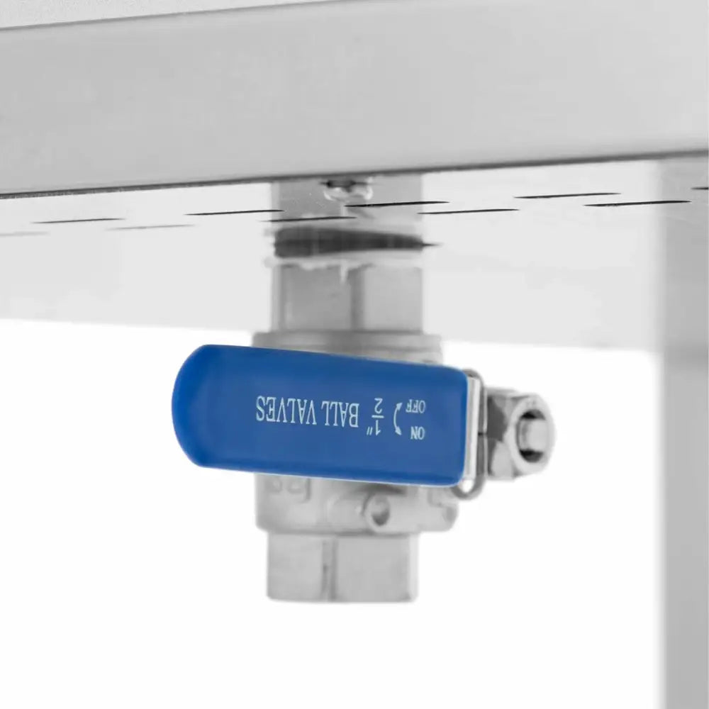 Kuleventil i stål med blått håndtak, sett fra siden under matvarmebrettets metallflate, viser ventilens detaljer.