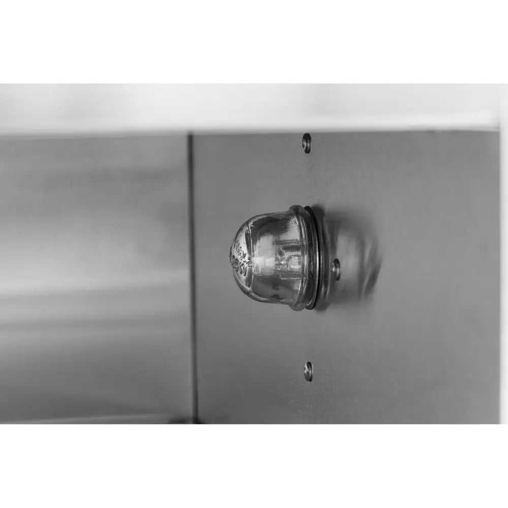 Glasslampe med kuppelform, nærbilde av innfatning og skruefester mot grå metallvegg.