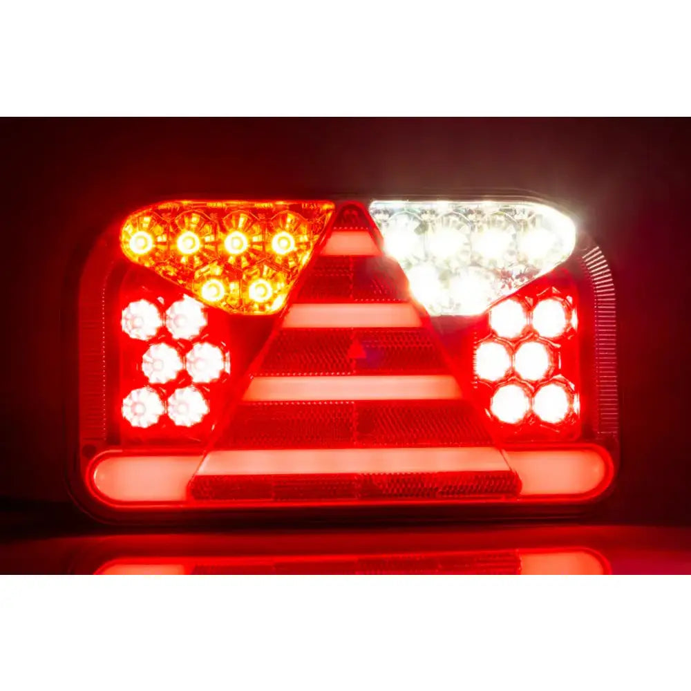 Baklys tilhenger venstre, frontbilde med tent LED i rødt, hvitt og oransje, trekantrefleks og runde lys.