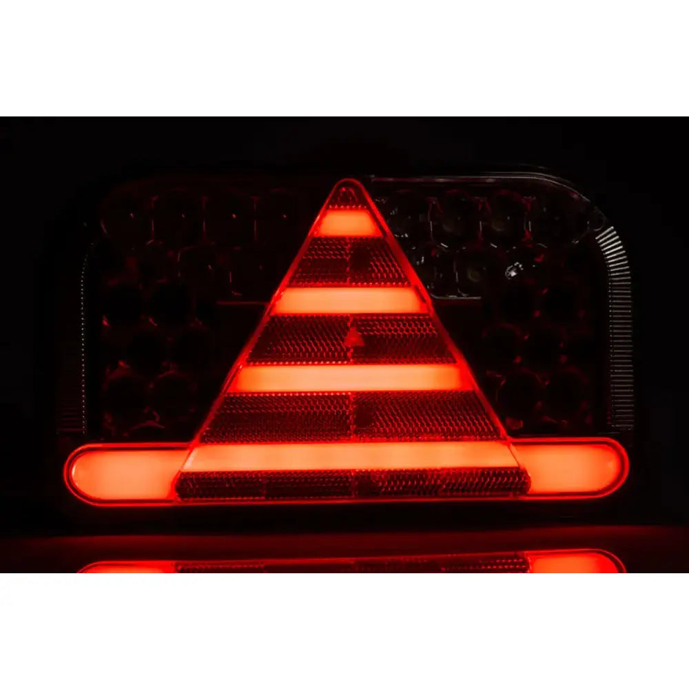 Baklys tilhenger venstre Fristom, frontbilde i mørke med klar rød trekant og horisontale lysstriper.