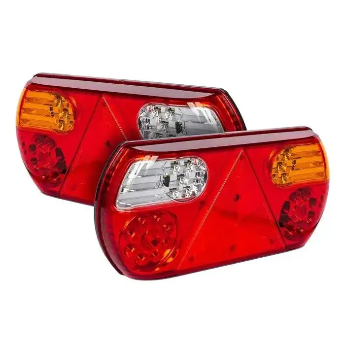 Baklys tilhenger Aspöck, to baklykter i klar plast med røde, oransje og hvite felt, sett fra skrå vinkel.