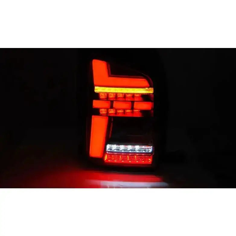 Baklykter Volkswagen T6 15-19 LED Black Smoke med opplyste røde og hvite felt sett forfra i mørket.