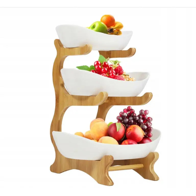 Bambus fruktholder med tre hvite keramiske skåler fylt med frukt, på lyst trestativ sett forfra.
