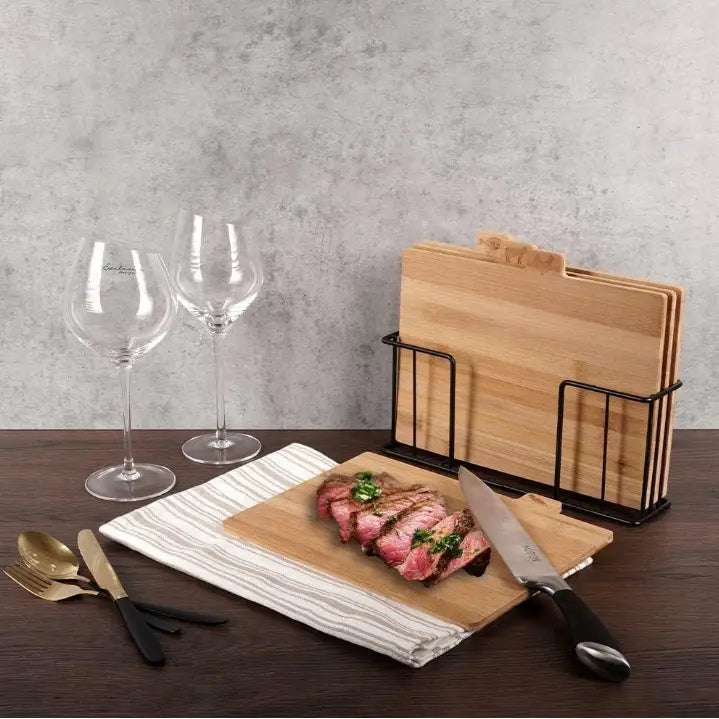 Bambuskjøkken skjærebrett sett, ett brett i bruk med biff og kniv, flere brett i stativ på spisebord.