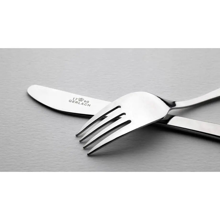 Barnebestikk i rustfritt stål, nærbilde av gaffel og kniv med gravert merke, krysset på lys bordflate.