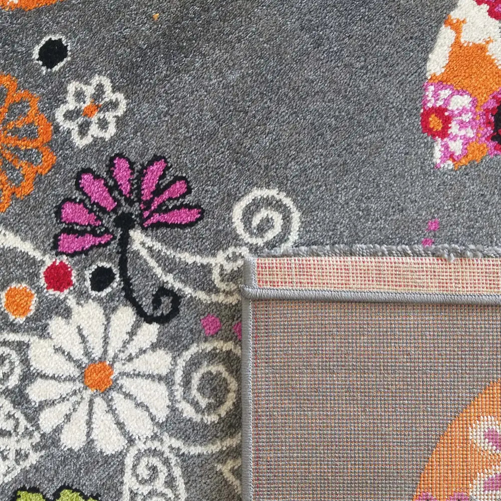 Bella 114 grå teppe, nærbilde av fargerike blomster og synlig bakside med detaljert kanting.