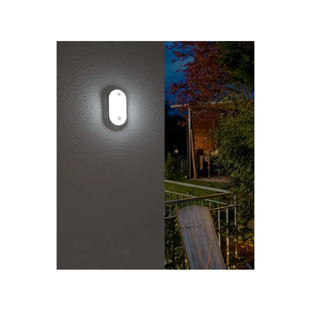 Belysningsarmatur med bevegelsessensor, hvit vegglampe lyser opp uteområde med hage og møbler i mørket.