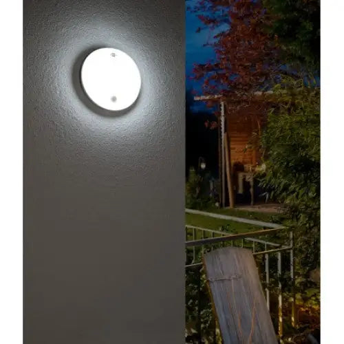 Oval LED utendørs vegglampe med bevegelsessensor, lyser opp fasaden i mørket med hage og terrasse bak.