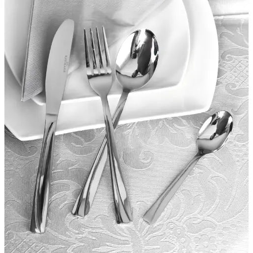Bestikksett i sølvfarget rustfritt stål, plassert på dekorert duk ved hvite tallerkener og serviett.