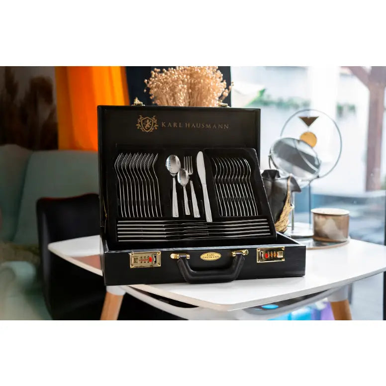 Bestikksett med 72 deler i sølv, organisert i åpen sort koffert med gullfargede detaljer, sett forfra på bord.