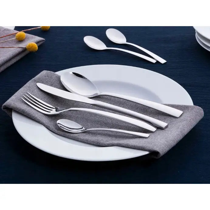 Bestikksett Future, fire blanke deler på grå serviett og hvit tallerken, to skjeer bak.