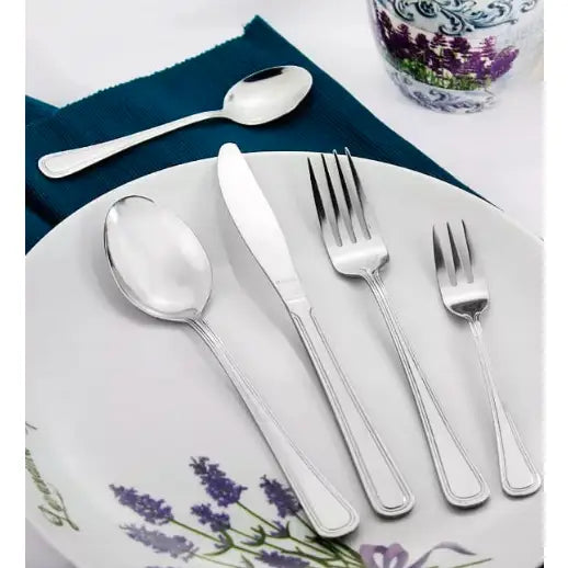 Bestikksett Bologna, fem deler i blankt stål på tallerken med lavendelmotiv og ekstra teskje på blå serviett.