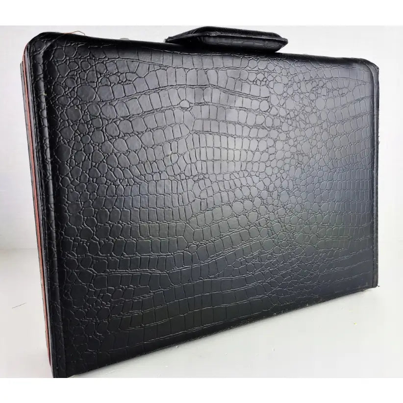 Svart mappe i imitert krokodilleskinn til bestikksett, sett fra siden med synlig håndtak på toppen.