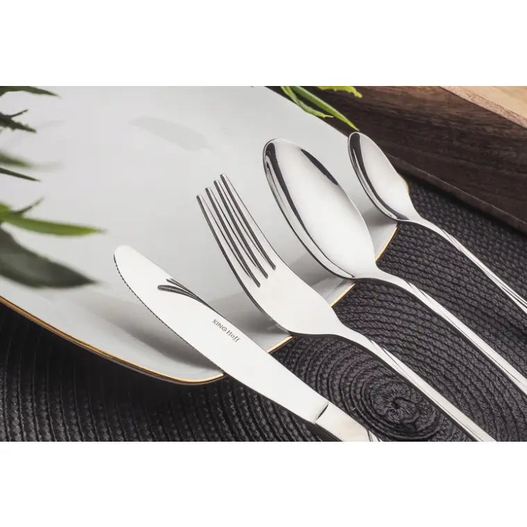 Bestikksett i rustfritt stål, fire blanke deler elegant lagt på gullkantet tallerken, sett fra skrå vinkel.