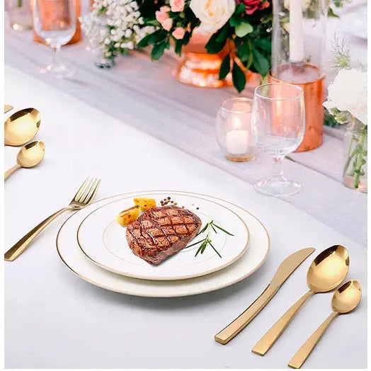 Bestikksett i gull, elegant oppdekket med kjøttrett, hvite tallerkener med gulldetaljer og festlig bordpynt.