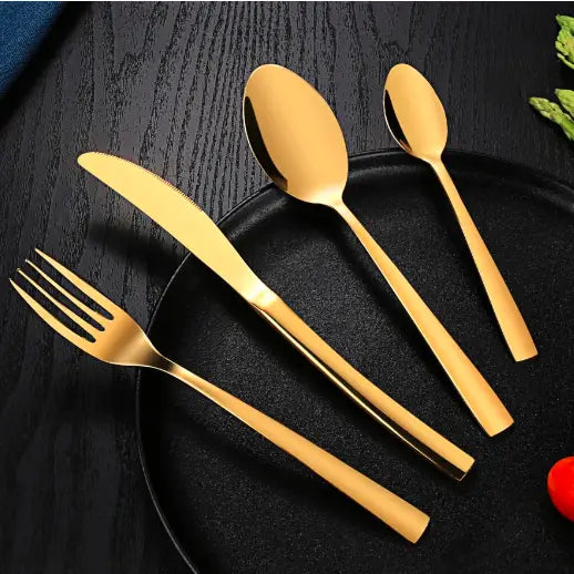 Bestikksett i gull, fire deler med moderne rette linjer, presentert på svart tallerken mot mørkt trebord.