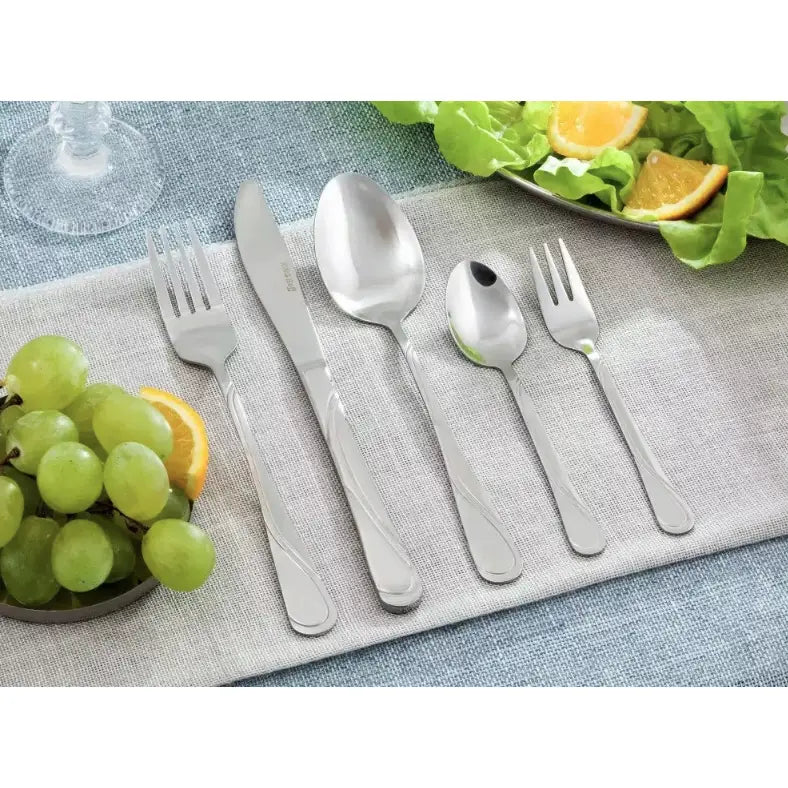Bestikksett Kinghoff, fem glansede deler i rustfritt stål på lys duk, med druer og salat bak.