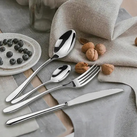 Bestikksett i rustfritt stål, fire blanke deler arrangert på grå duk med nøtter og blåbærfat ved siden av.
