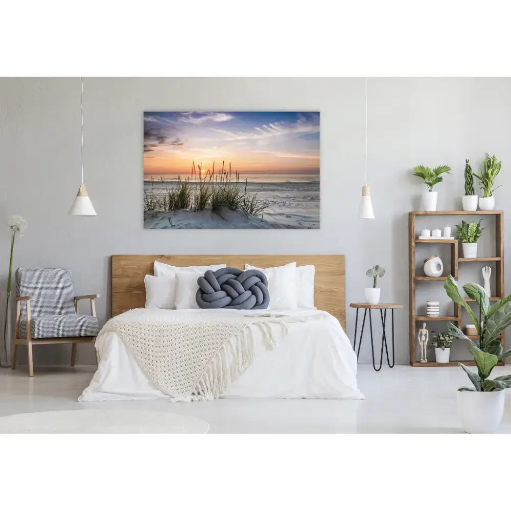 Lerretsbilde med strand og solnedgang på sengevegg, omgitt av moderne, lyse møbler og grønne planter.