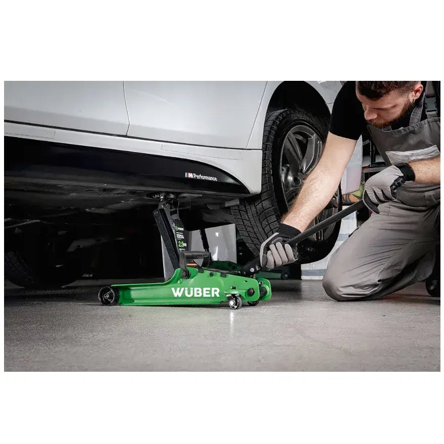 Biljekk Lavprofil 2,5t, grønn hydraulisk jekk i bruk under bil av person med hansker på verkstedgulv.