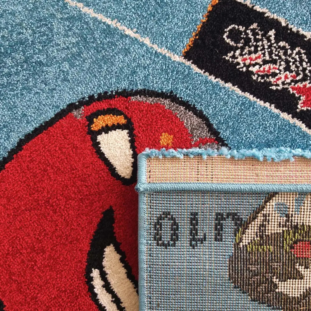 Blå Bella Tepe, nærbilde som viser tegneseriemotiv og oppbrettet hjørne for detaljer av bakside og kant.