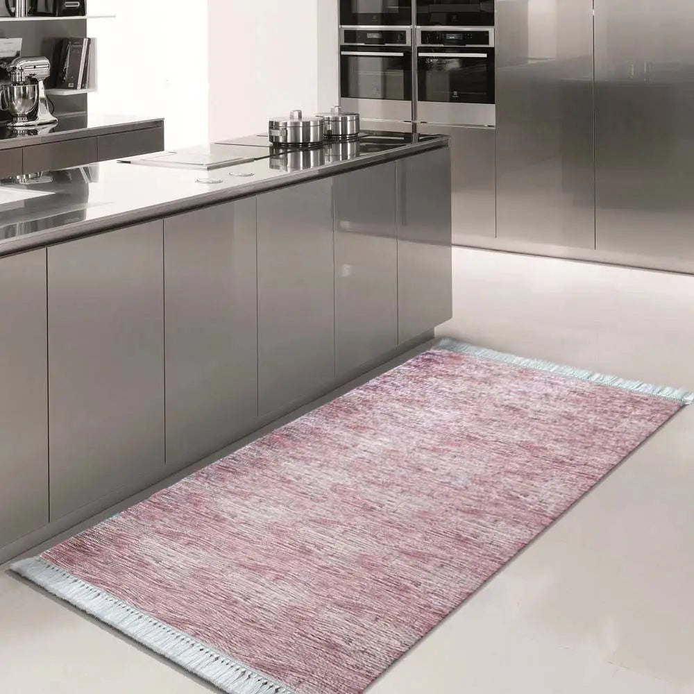 Blanka 03 teppe i pudderrosa, rektangulært med lyse frynser, foran grå kjøkkeninnredning på lyst gulv.