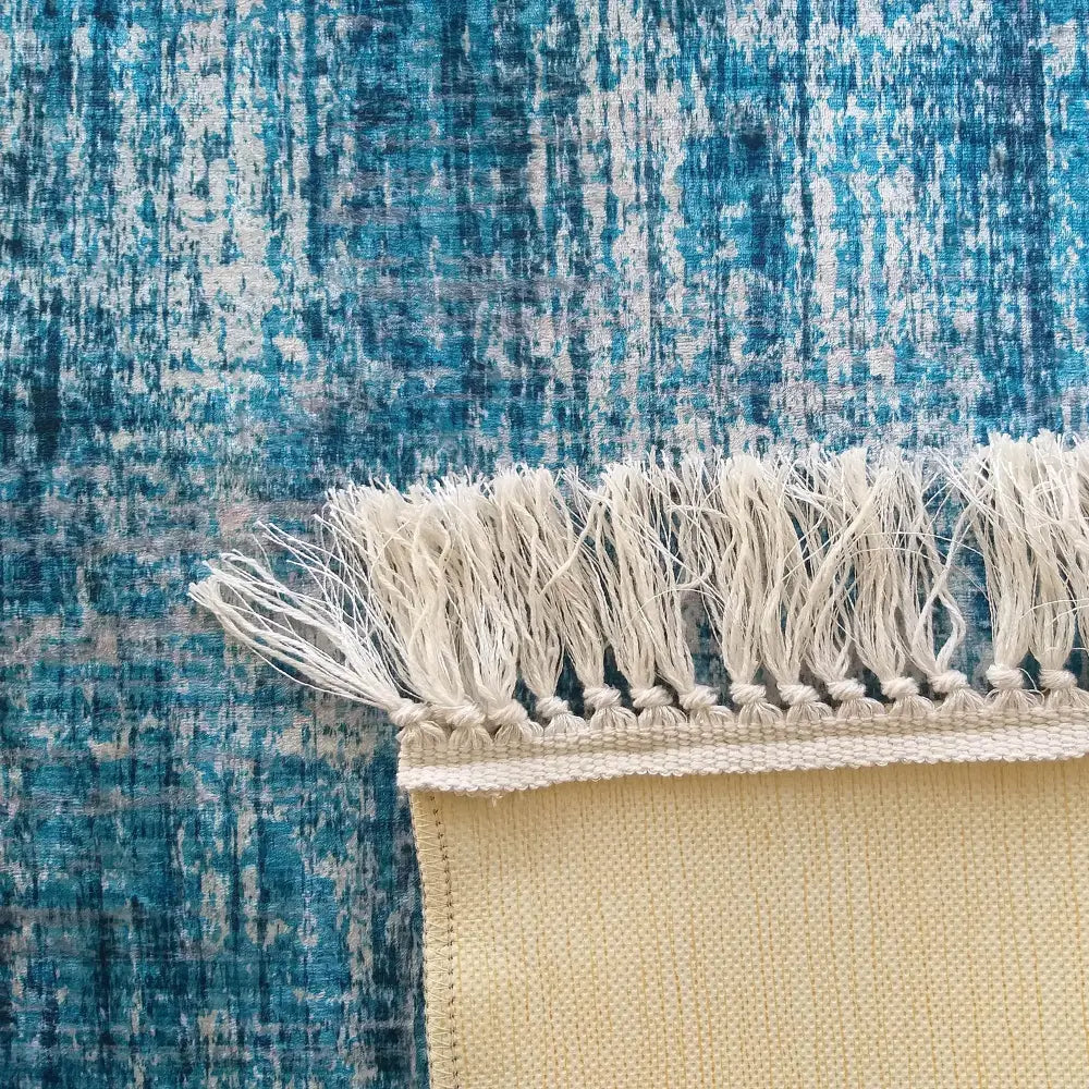 Blått teppe 160 x 220 cm fra Blanka, nærbilde av hjørne med kremfargede frynser og tydelig tekstur.
