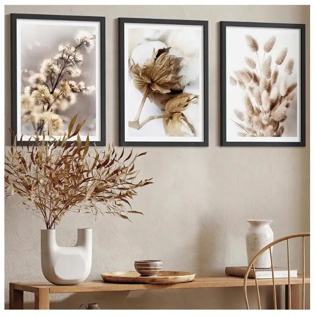 Boho blomster tryptyk, tre botaniske bilder i sort ramme over lyst trebord med vaser og tørkede blader.