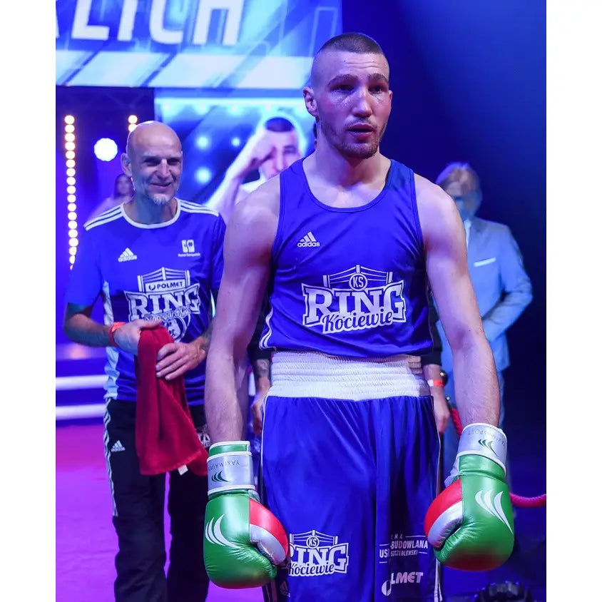 Boksehansker GRAND i grønt ekte skinn, brukt av bokser i blå sportsdrakt i opplyst boksearena.