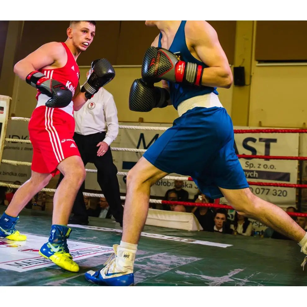 To boksere i ringen med PRO SPIDER boksehansker i aksjon, dommer og publikum synlige bak.