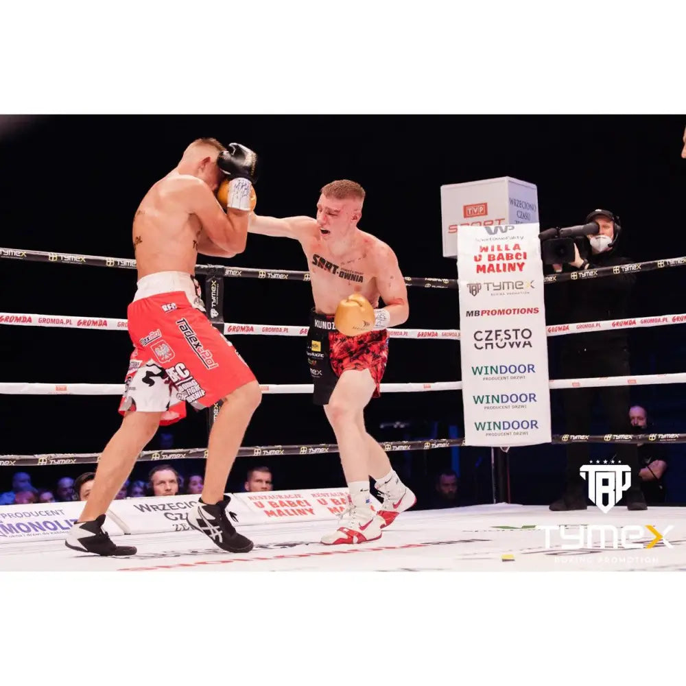 Boksehansker TIGER GOLD i bruk under boksekamp, to boksere i aksjon med tilskuere og sponsorskilt bak.