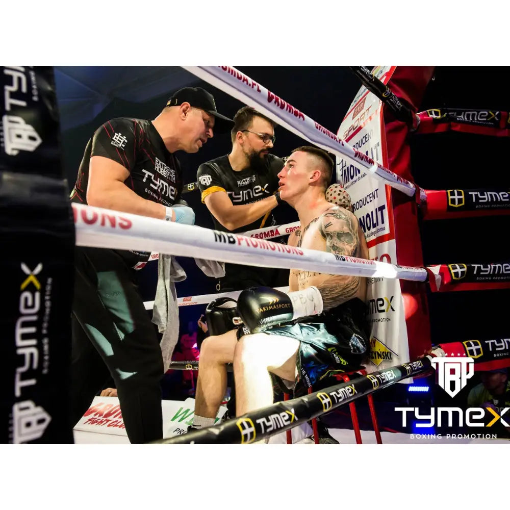 Boksehansker TIGER GOLD L 8 oz i bruk, bokser hviler i ringen omgitt av lagmedlemmer under kamp.