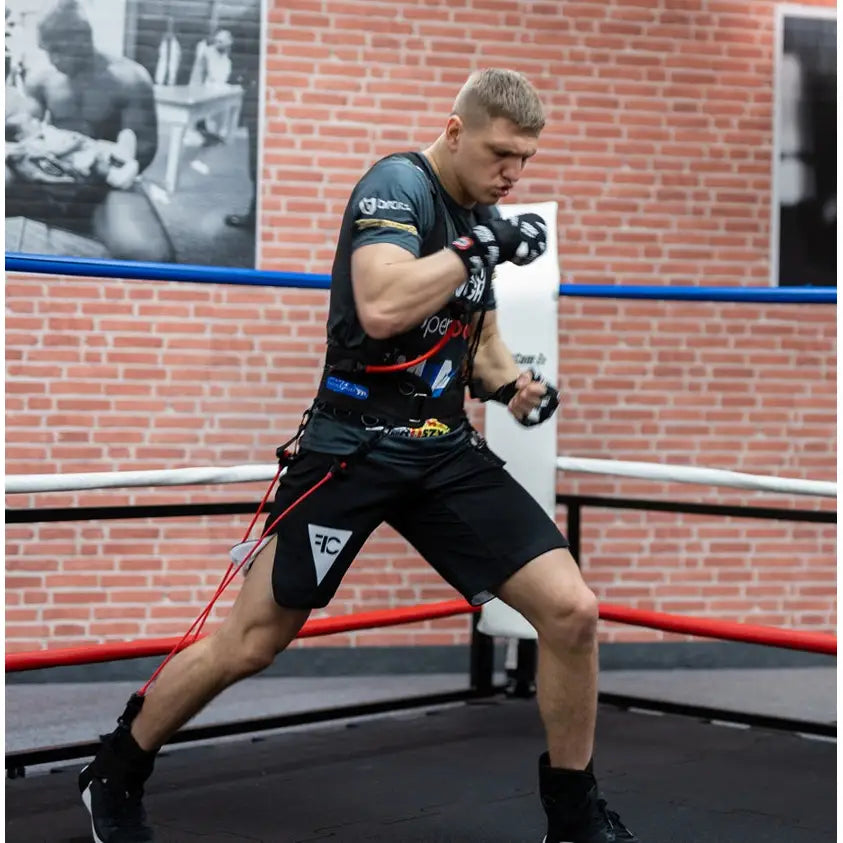 Boksetrening Kaugummi, mann med motstandsbånd rundt livet og føttene, sideprofil i boksering med mursteinsvegg.